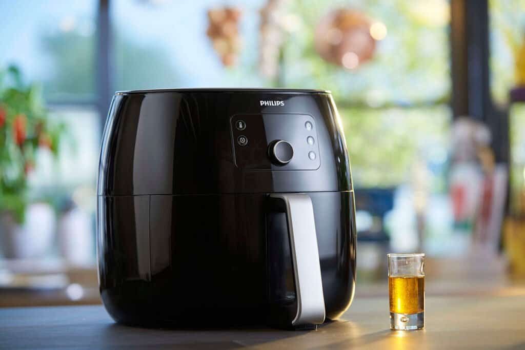 Modern black air fryer on kitchen counter with a small glass of oil beside it.